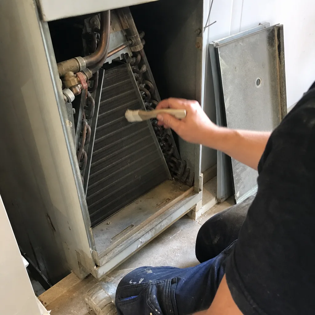 HVAC technician cleaning cooling coils inside an air conditioning unit